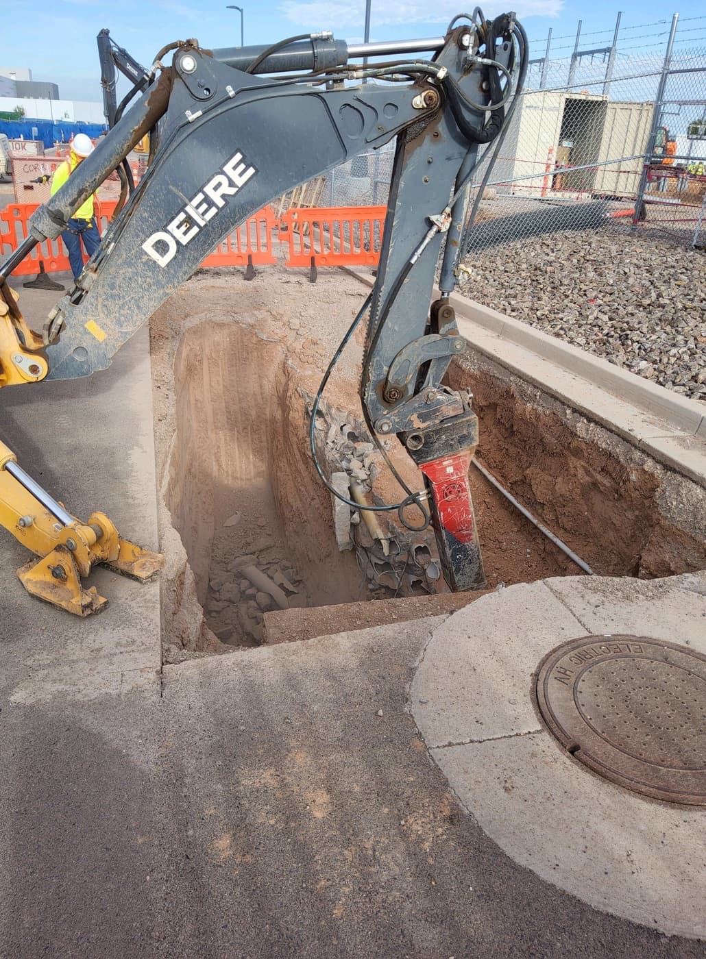 Excavator digging a utility trench beside a substation fence